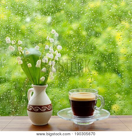 A cup of coffee and lilies of the valley on the window. Rain drops on the window.