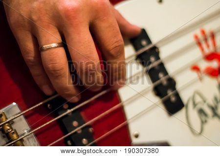Bass Guitar In Playing Musician Hands Close-up. Focus On Bass Guitar Neck In Player Hands. Unrecogin