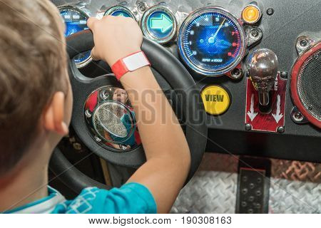 Little boy at the wheel of the car simulator with his back to the camera