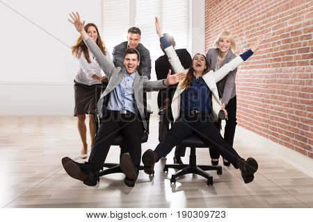 Smiling Businesspeople Playing Together With Swivel Chair In The Office