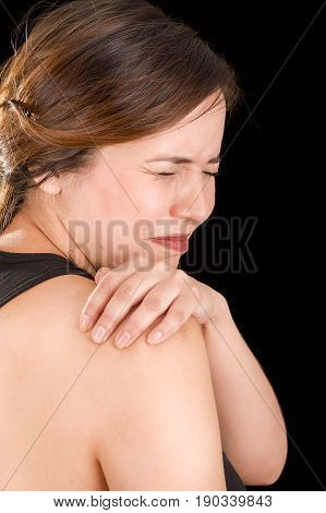 Close up of a beautiful young woman suffer from shoulder pain in a black background.
