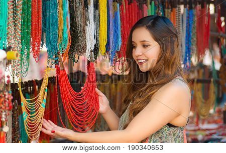 Beautiful caucasian woman holding a finished traditional necklace in her hands and smiling to the camera, handicrafts art, colorful necklace background.