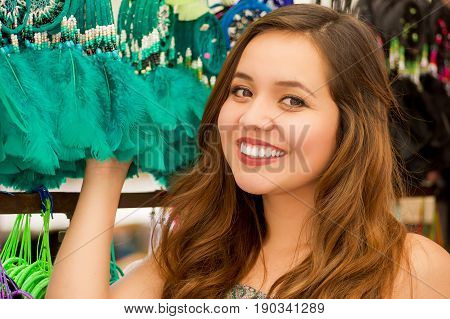 Close up of a beautiful smiling young woman touching a colorful catchdreamers, in colorful market fabrics background.