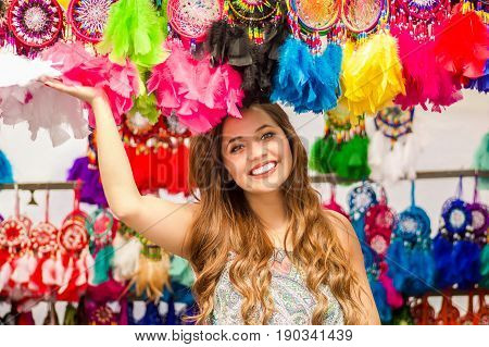 Beautiful smiling young woman touching a colorful catchdreamers, in colorful market fabrics background.