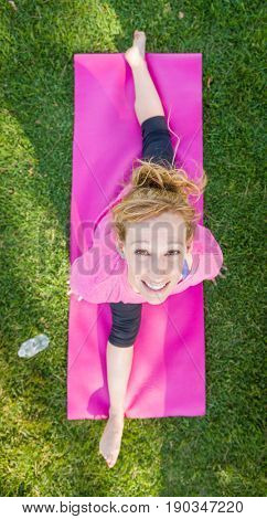 Overhead of Young Fit Flexible Adult Woman Outdoors on The Grass With Yoga Mat Doing The Splits.
