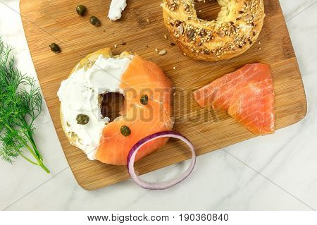 Bagel ingredients. Lox, purple onions, capers, dill, and the buns, shot from above on a wooden board and a white marble background in the process of making, with a place for text
