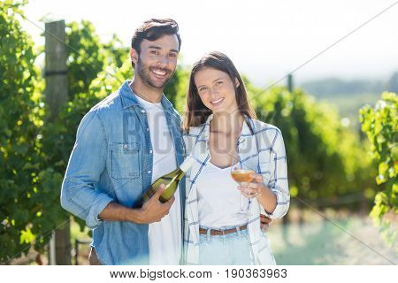 Portrait of smiling couple with wine standing at vineyard