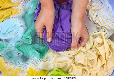 Female hands wash colored clothes in basin.