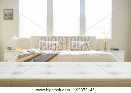 White leather empty bench in front of defocused bedroom in yellow and beige colors in background. Display of products.
