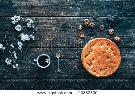 Mug of coffee and homemade cake with nuts and chocolate on old wooden Board and flowering branches of peach in springtime.