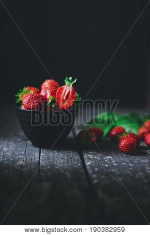 Strawberry in a bowl with leaves on an old wooden board