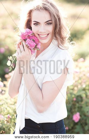 Smiling blonde girl 14-19 year old holding roses in field. Looking at camera. Summer time.