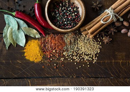 Pepper In Bowl With Scattered Herbs And Spices, Laurel Leaves, Chili Peppers On Wooden Tabletop