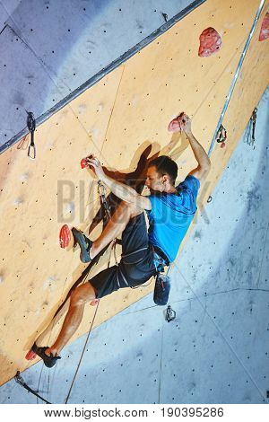 man climber climbs with rope on climbing gym. man mekes hard wide move. Climbing competition