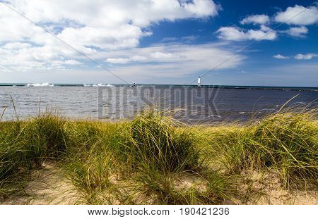 Summer Beach Panorama. Dune grass on the beach with sunny blue sky and lighthouse in the background on the Lake Michigan coast. Frankfort, Michigan.