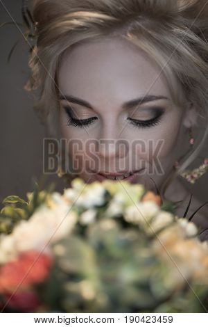 Happy beautiful bride with bright make-up and voluminous hairdress looks at her bright bouquet and smiles