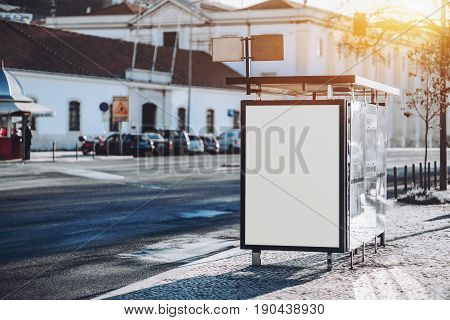 Mock-up of empty billboard inserted in glass bus stop vertical blank poster near city road white information placeholder in urban settings with copy space for logo text or other advertising