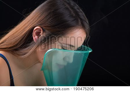 Young woman doing inhalation with a medical vaporizer nebulizer machine on black background.