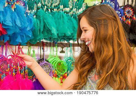 Close up of a beautiful smiling young woman touching a colorful catchdreamers, in colorful market fabrics background.