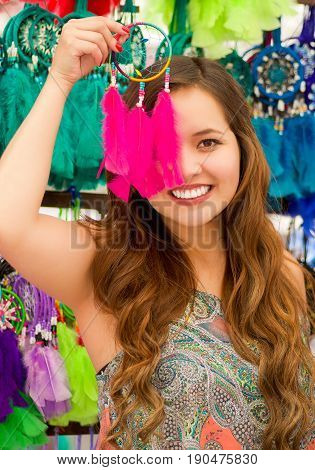 Beautiful smiling young woman pointing in from of her face a pink catchdreamers, in colorful market fabrics background.