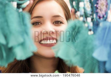 Close up of a smiling woman hiding behind a magenta catchdreamer, in colorful market background