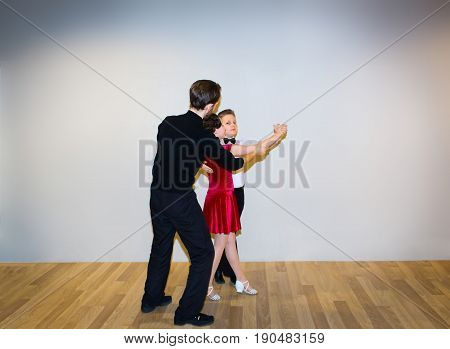 The young boy and girl with male coach or teacher posing at dance studio on gray. The ballroom dancing school and education concept