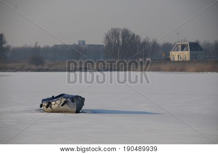 A small boat is lying on a frozen canal near Amsterdam, the Netherlands