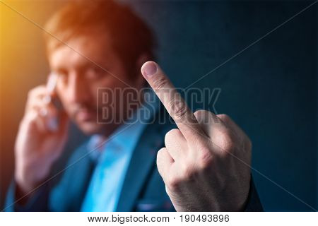 Rude businessman talking on mobile phone and giving middle finger gesture as sign of agreement refusal job quitting or displeased reaction