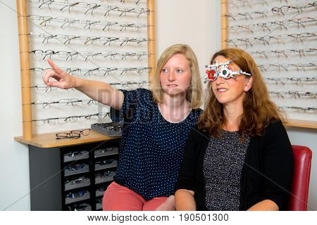 Female Optican Checking Eyes Of Woman For New Glasses