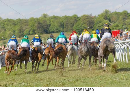 STOCKHOLM SWEDEN - JUNE 06 2017: Rear view of standing colorful jockeys on gallop race horses riding in a curve at Nationaldags Galoppen at Gardet. June 6 2017 in Stockholm Sweden