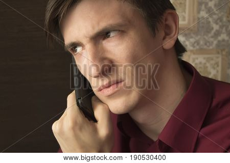 A young man in a purple shirt is waiting for an answer on a smartphone, with an alarming suspicious look, frowning