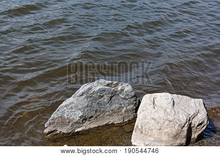 Large Rocks Near The Shore Lapped By The Waves Of The Lake