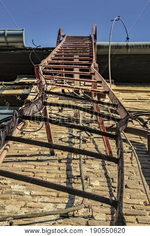 Damaged, deformed metal ladder on the side of an old industrial building