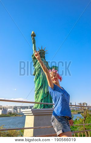 Happy tourist woman enjoying indicating Statue of Liberty, icons of Odaiba Island in Tokyo, Japan. Female lifestyle smiling while on a trip out of Tokyo in popular Odaiba. Summer vacation in Japan.