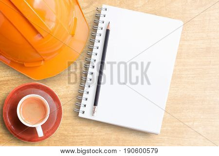 Safety helmet and cup of coffee with notebook on wooden table. top view with copy space