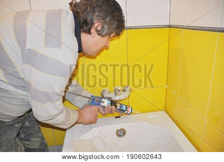KIEV - UKRAINE JUNE - 19 2017: Bath tube installation with Silicone Bathroom Caulk water tap in the yellow tiled bathroom. Repair bathroom with new bath tube. Silicone a Bath with Caulking Gun