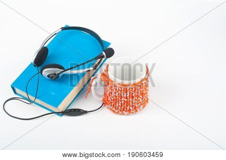 Audiobook on white background. Headphones put over blue hardback book, empty cover, copy space for ad text. Distance education, e-learning concept