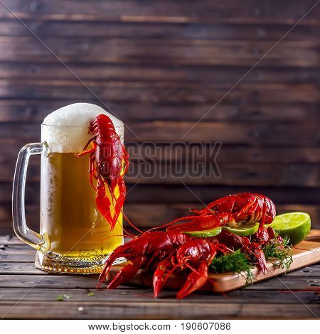 Glass of beer on a wooden background. Nearby boiled crayfishes with greens and lime. Snack to beer. Summer atmosphere. Selective focus