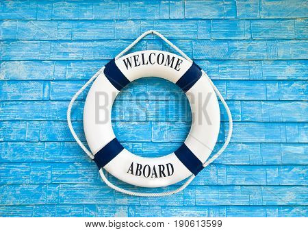 White color Life buoy with welcome aboard on it hanging on blue wall