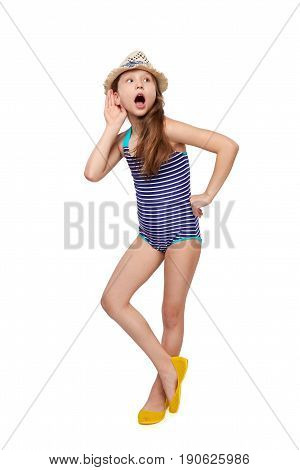 Surprised full length child girl in swimsuit and summer hat with hand on ear listening, over white background