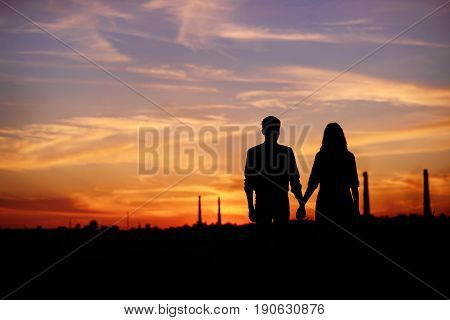 Young Couple Is Holding Hands On A Background Sunset Silhouette