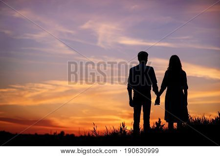 Young Couple Is Holding Hands On A Background Sunset Silhouette