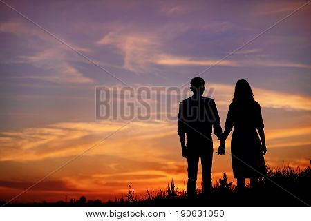 Young Couple Is Holding Hands On A Background Sunset Silhouette