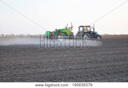 KIEV - UKRAINE JUNE - 19 2017: Tractor fertilizer tank with fertilizer from the sprinkler spray. Tractor Mounted Tank Sowing and Plowing action on the corn field in spring sunset.