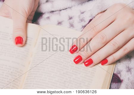 woman manicured hand with red nails read the book wrapped in a blanket