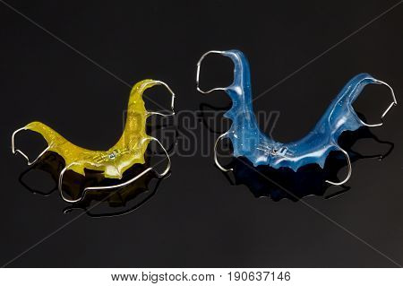 Colorful dental braces or retainers for teeth on black glass background closeup