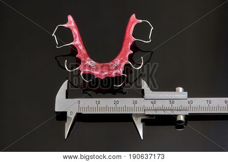 Colorful dental braces or retainers for teeth on black glass background and vernier caliper closeup