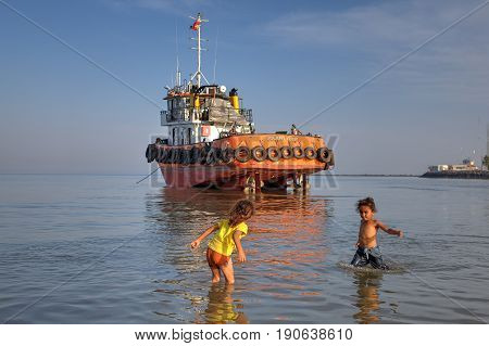 Bandar Abbas Hormozgan Province Iran - 16 april 2017: Two little girls about seven years old play in the water near the shore against the background of an industrial boat that ran aground.
