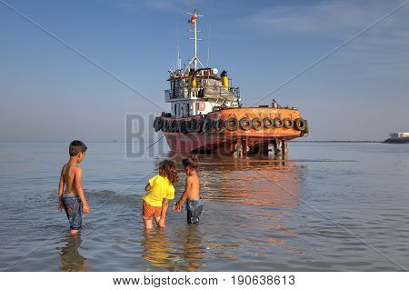 Bandar Abbas Hormozgan Province Iran - 16 april 2017: Three young children about 7 years old two little girls and one boy playing in the water of the Persian Gulf near the jammed boat.