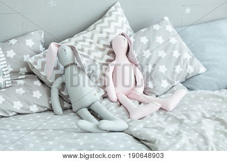 Cute grey and pink bunnies toy on bed in baby room
